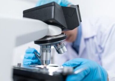 Male scientist observing a blood sample through a microscope.