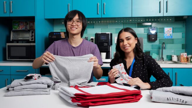 Two volunteers placing tshirts in a gift bag for blood donors.